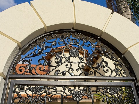 Stone archway and wrought iron gate in front of Spanish architectural designed home.