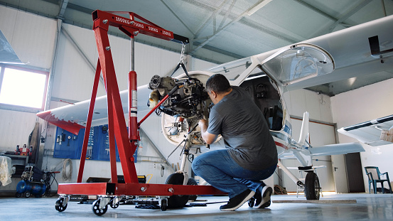 Airplane engineer working in an airport hangar checking on aircraft engine before  putting it back to flight.