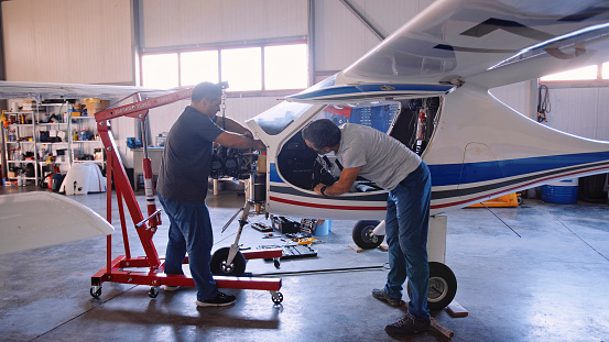 Airplane engineers working in an airport hangar checking on aircraft engine before  putting it back to flight.