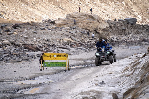 Manali, India - circa 2023: crowd of people at lahul spiti showing small food outlets, adventure sports with family riding ATV on the snow covered road with himalay peaks in the distance