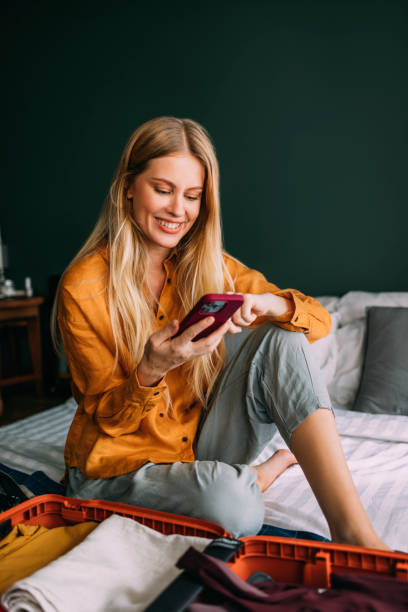 istock A Happy Beautiful Blonde Woman Watching Something On Her Mobile Phone While Packing Her Suitcase For A Business Trip 1477307915
