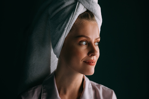A portrait of a pensive Caucasian female with her hair wrapped up in a towel relaxing after taking a shower.