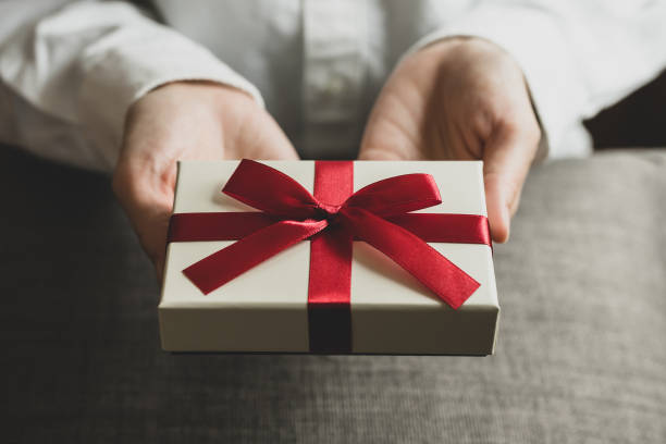 Female hand holding present box with red ribbon