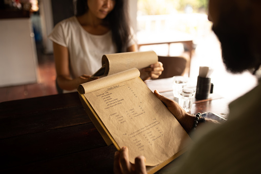 Male and female reading from a menu's what to order, while siting in cafe.