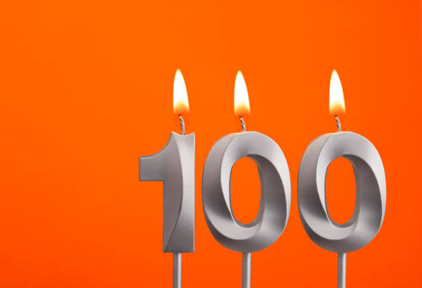 istock Number 100 - Silver Anniversary candle on orange background 1477320654