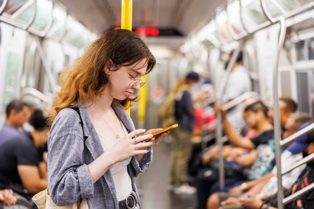 jeune femme rousse lisant des messages sur son smartphone dans un wagon de métro plein contre des personnes floues - subway station subway train new york city people photos et images de collection