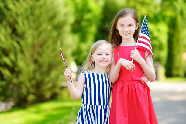 two adorable little sisters holding american flags outdoors on beautiful summer day. - child flag fourth of july little girls imagens e fotografias de stock