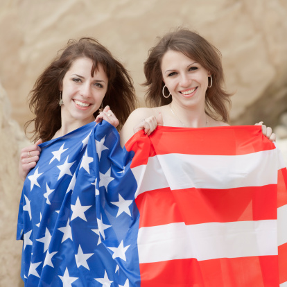 Two attractive brunettes are posing with American flag looking at camera smiling