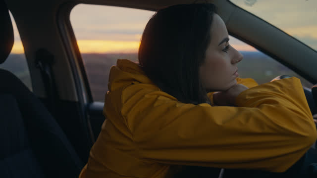 Alone with Her Thoughts: Young Woman Leans on Car Steering Wheel at dawn