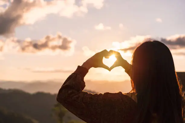 Photo of Young woman traveler making heart shape symbol at sunrise over the mountains and looking beautiful landscape, Travel lifestyle concept