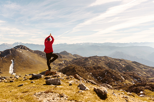 man on his back in red clothes and arms raised, practicing yoga with the tree pose and contemplating the mountain landscape after hiking up a mountain. sport, travel and adventure. meditation.
