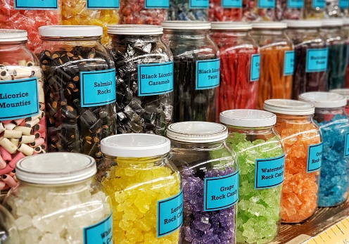 Old fashioned New England candy store has more candy choices than I ever even knew was possible! Close up of a large collection of retro style glass jars filled with delicious house-made confections abundantly lining the walls atop wooden shelves for eager customers, young and old.