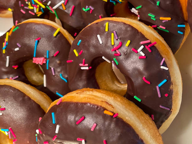 istock Full frame image of rows of chocolate fondant iced ring doughnuts topped with multicoloured sugar sprinkles, being served at hotel self service buffet, elevated view, focus on foreground 1477389182