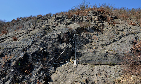 reinforcing slope with a steel net anchored deep into rock. rows inclined fences with massive netting above mountain pass will hold back large eroding boulders and falling stone, steel frame, circle, anchoring, stabilization, reinforcing, screwed