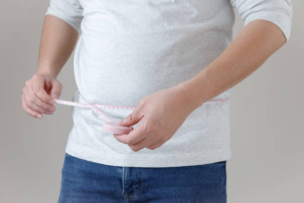 un hombre que lleva una camiseta y jeans está midiendo el tamaño de su cintura, lo que implica una imagen de gestión de la salud y dieta. - síndrome metabólico fotografías e imágenes de stock