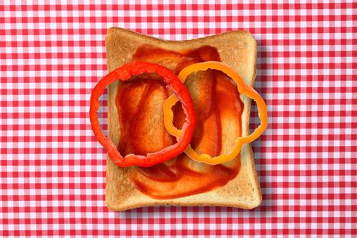 Overhead shot of toasted bread with tomato sauce and bell pepper on gingham check tablecloth.
