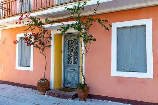 A colorful, beautiful Greek house front with a traditional door, windows and decorated with flowering plants.