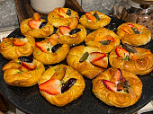 Close-up image of freshly baked breakfast Danish pastries at hotel restaurant buffet, rows of pastries topped with fruit slices stacked on marble platter, elevated view, focus on foreground