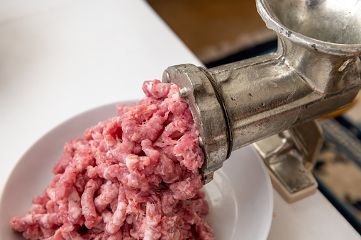 Mincing pork meat with a manual mincer at home.