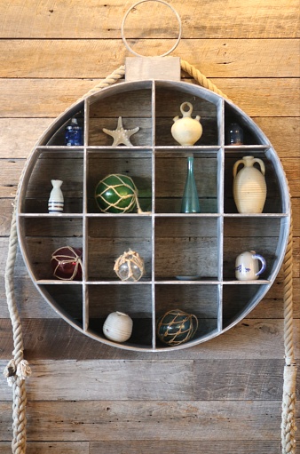 While on a vacation in Maine, I spotted this beautiful and simple nautical wall decor. It was probably had a three four foot circumference or so; isn't she grand? Metal Shelf with thick rope accents, houses many nautical themed individual pieces, with a rustic natural wood wall behind it.