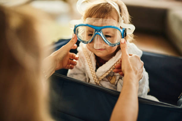 Cute baby girl whit diving mask sitting in suitcase at home