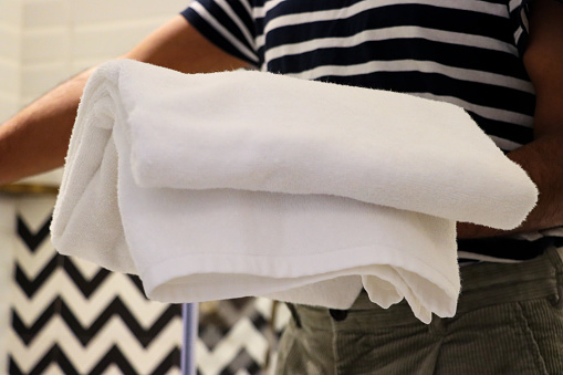 Stock photo showing close-up view of pile of folded, white towels being carried by an unrecognisable person in a luxury hotel bathroom with black and white zig-zag patterned wall tiles. Home furnishings and bedroom interior design.