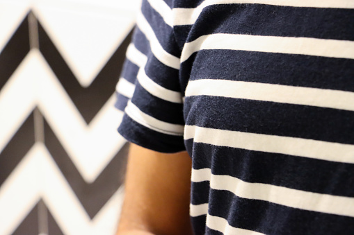 Stock photo showing close-up view of an unrecognisable person wearing a navy and white striped T-shirt in a luxury hotel bathroom with black and white zig-zag patterned wall tiles. Home furnishings and bedroom interior design.