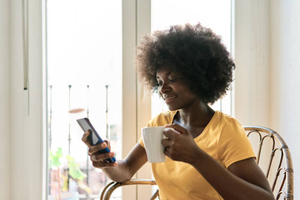 istock Woman with afro hairstyle using mobile phone and drinking coffee 1477410983