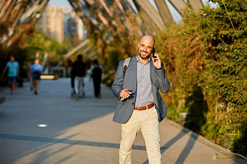 Front view of bearded man in business attire commuting from the office on foot and talking with caller in afternoon sunshine.