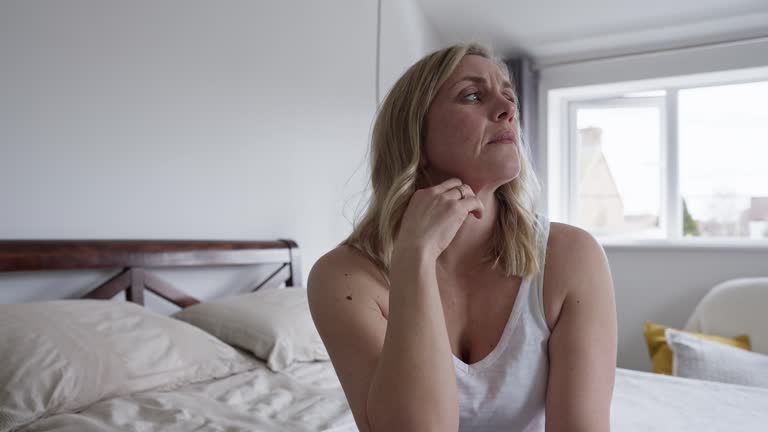 Menopausal Mature Woman Suffering With Low Mood And Anxiety Sitting On Bed At Home