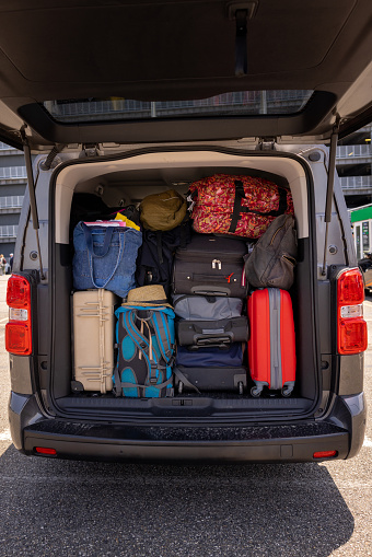 An open rental van boot filled with suitcases and luggage, loaded and ready for the return home after a holiday. The van is parked in an airport car park in Toulouse, France.