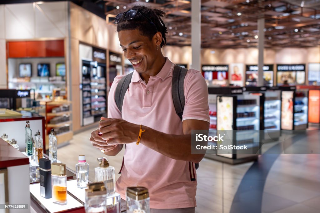 Duty Free Shopping A side-view shot of a young man wearing casual clothing exploring a duty free shop in an airport in Toulouse, France before catching his flight. The man is smelling aftershave. Perfume Stock Photo