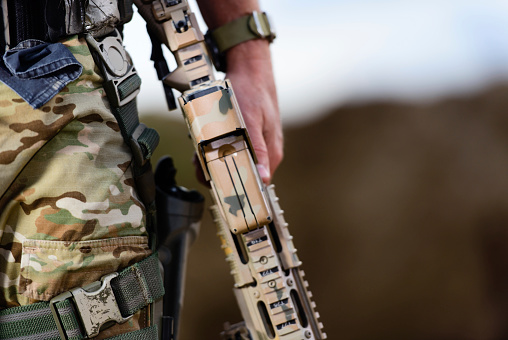 Close-up of assault rifle in hand by soldier's side.