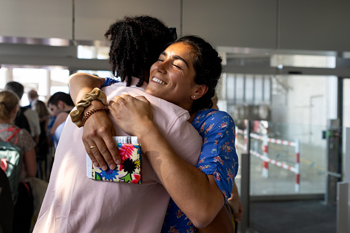 A close up shot of a young man and woman standing in a queue in an airport departure area in Toulouse, France waiting to get on their flight. The young man and woman are sharing a hug and smile.
