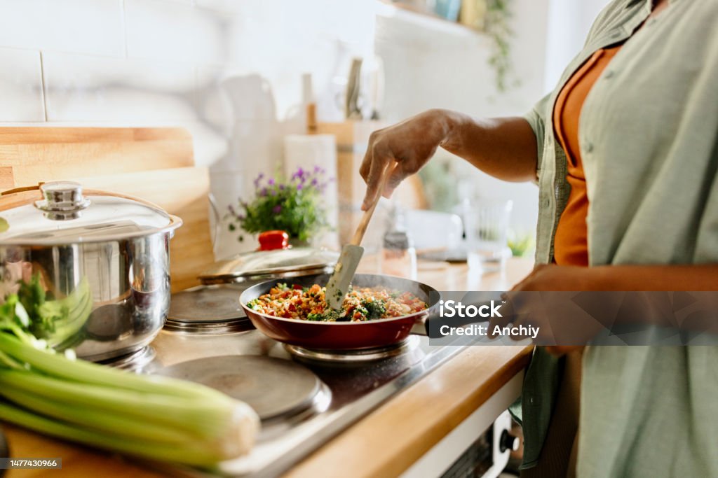 Woman preparing quinoa vegetable mix cooked in a frying pan Woman cooking a colourful and nutritious quinoa stir-fry with mixed vegetables and a drizzle of olive oil. Cooking Stock Photo