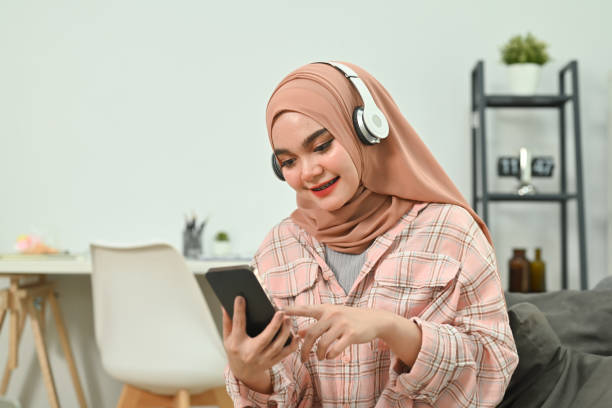 istock Pleasant young Muslim woman relaxing on couch texting messaging, browsing wireless internet on smartphone. 1477431272