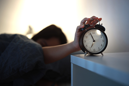 Young asian girl wake up early in morning, lying on bed and trying turn off alarm clock in bedroom at home