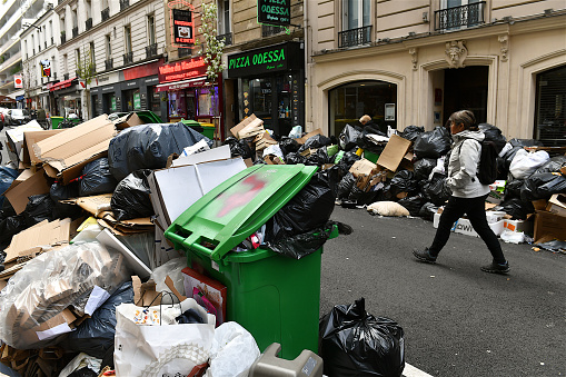 Paris, France-03 27 2023: Pedestrian passing through heaps of garbage overflowing on a Parisian sidewalk due to the garbage collectors' strike, France.