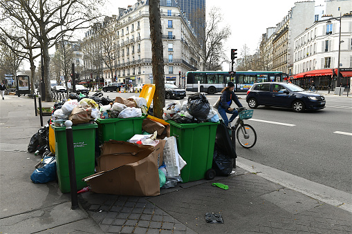 Paris, France-03 27 2023: Cars and cyclist passing near a pile of garbage overflowing on a Parisian sidewalk due to the garbage collectors' strike, France.