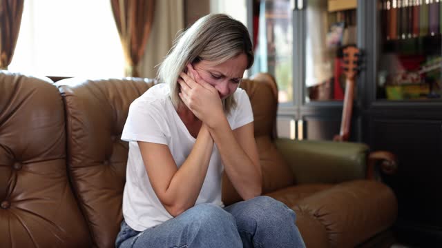 Lonely woman rubs face with hands sitting on sofa in room