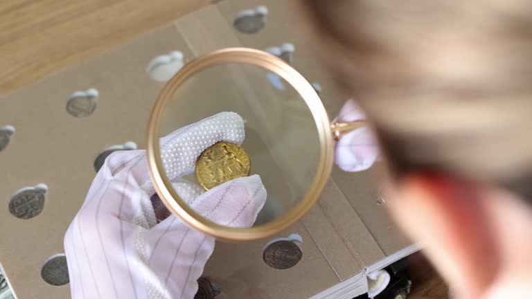 Woman in gloves looks at golden coin through magnifier glass