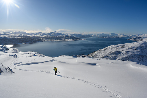 Distant view of ski mountaineers ascending snowcapped mountain across glacial plain