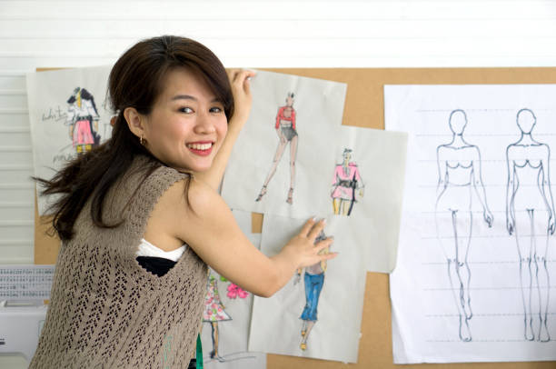 istock Young fashion designer paste pattern for cloth on cork board. Asian woman working in home base cloth design business. 1477440192