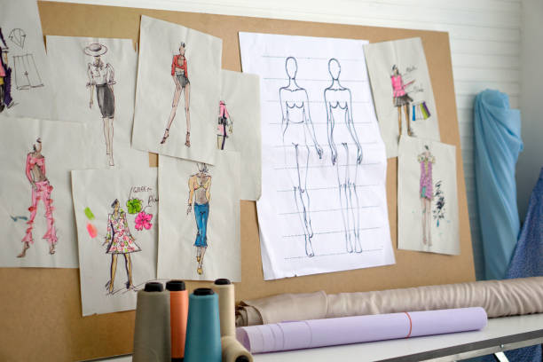 istock Pattern for cloth are pasted on the board in the sewing room. Rolls of cloth and multi-colored threads are on the table. Fashion designer room. 1477440195