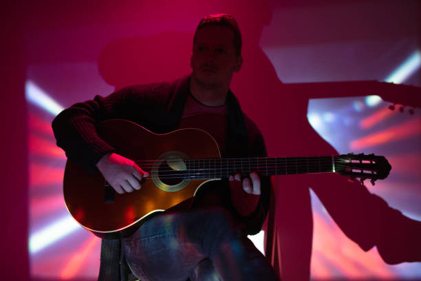 muzyk grający na gitarze akustycznej w mglistym klubie z kolorowymi światłami. - fingerstyle zdjęcia i obrazy z banku zdjęć