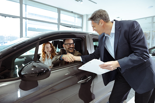 Happy couple and car salesperson talking in car dealership