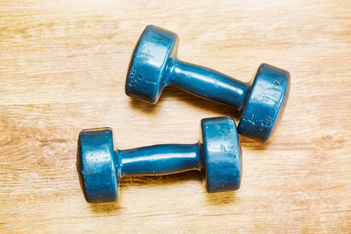 Medium-weight dumbbells, worn and well-used, on a surface with rich wood grain.
