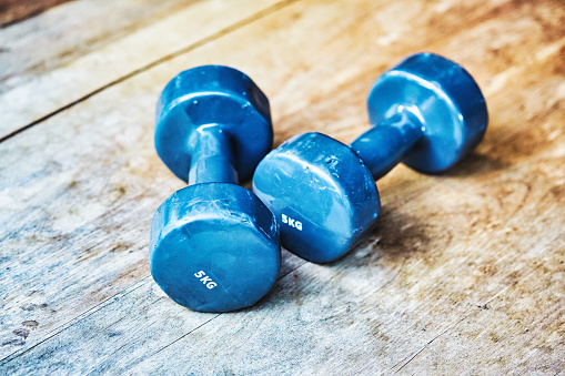 Medium-weight dumbbells, worn and well-used, on a weathered surface with rich wood grain.