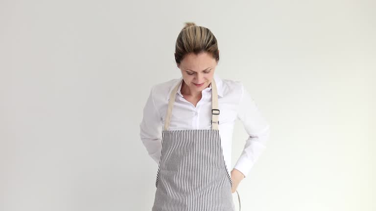 Female waiter putting on gray apron on white background 4k movie slow motion