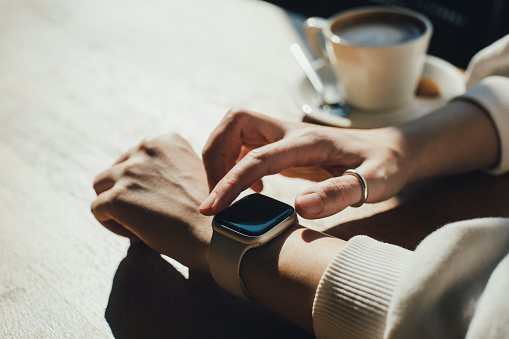 Woman's hands using a smart watch with a mug of fragrant coffee on a background in a cafe.